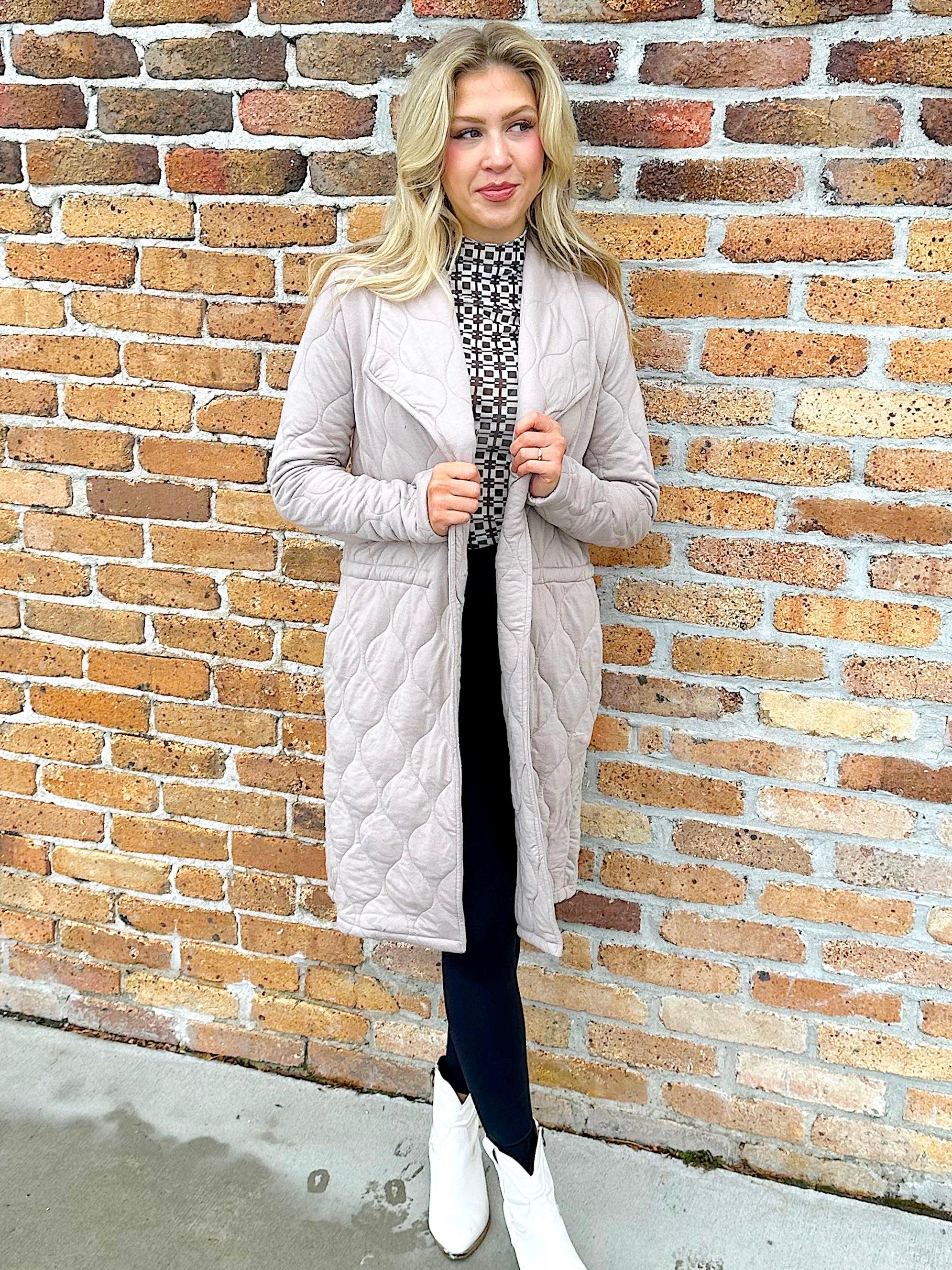 woman wearing quilted taupe long jacket. brand Steve Madden with a drawstring to cinch at waist for more fitted apperance
