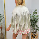 Woman wearing white faux leather fringe jacket with floral hem detail, viewed from behind, styled with white cowboy boots.