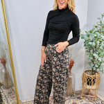 Wide-leg floral denim pants in black with muted rose and taupe blooms, styled with black turtleneck.