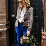 Woman wearing cropped plaid houndstooth jacket with satin panels over white button-down and blue flare jeans