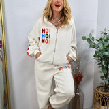 Cream zip-up hoodie with colorful "HO! HO! HO!" chenille lettering, styled with matching jogger sweatpants.