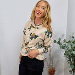Cream floral print pullover sweater styled with dark jeans and pearl necklace, worn by smiling blonde woman.
