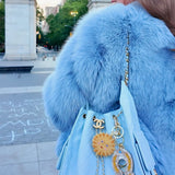 Light blue quilted Chanel bag with sun-face and horseshoe keychains, paired with fluffy blue fur coat.