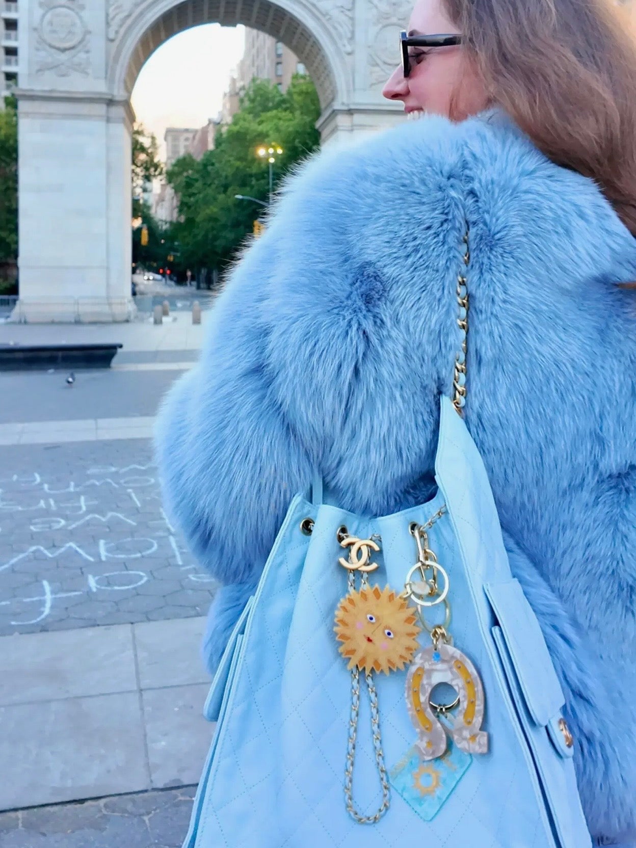 Light blue quilted Chanel bag with sun-face and horseshoe keychains, paired with fluffy blue fur coat.