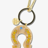 Solar eclipse horseshoe keychain in beige acrylic with gold star details, blue dot accents, and gold carabiner clip.