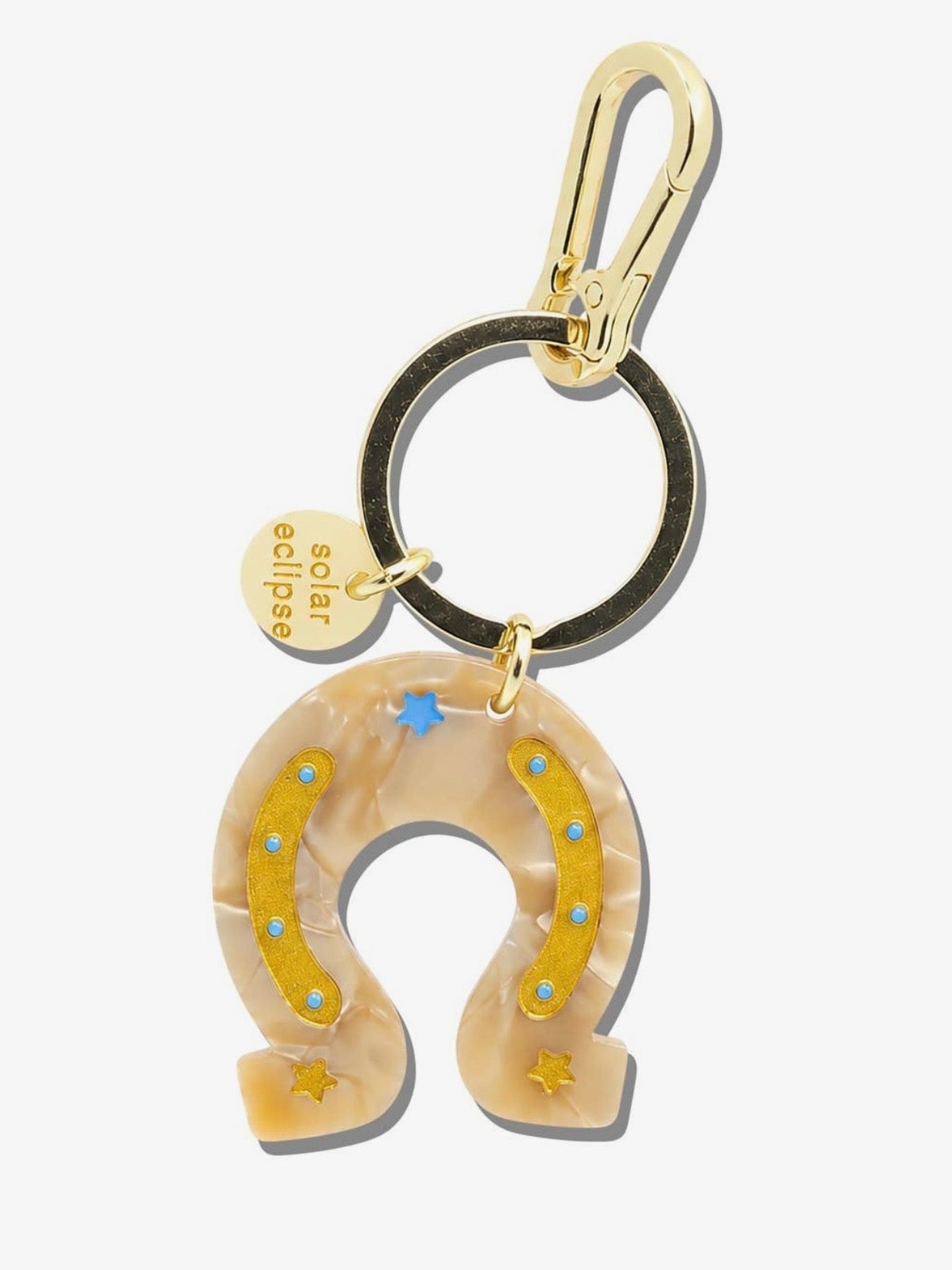 Solar eclipse horseshoe keychain in beige acrylic with gold star details, blue dot accents, and gold carabiner clip.