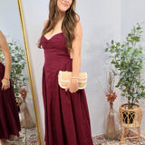 Woman wearing a strapless plum midi dress with sweetheart neckline and woven clutch