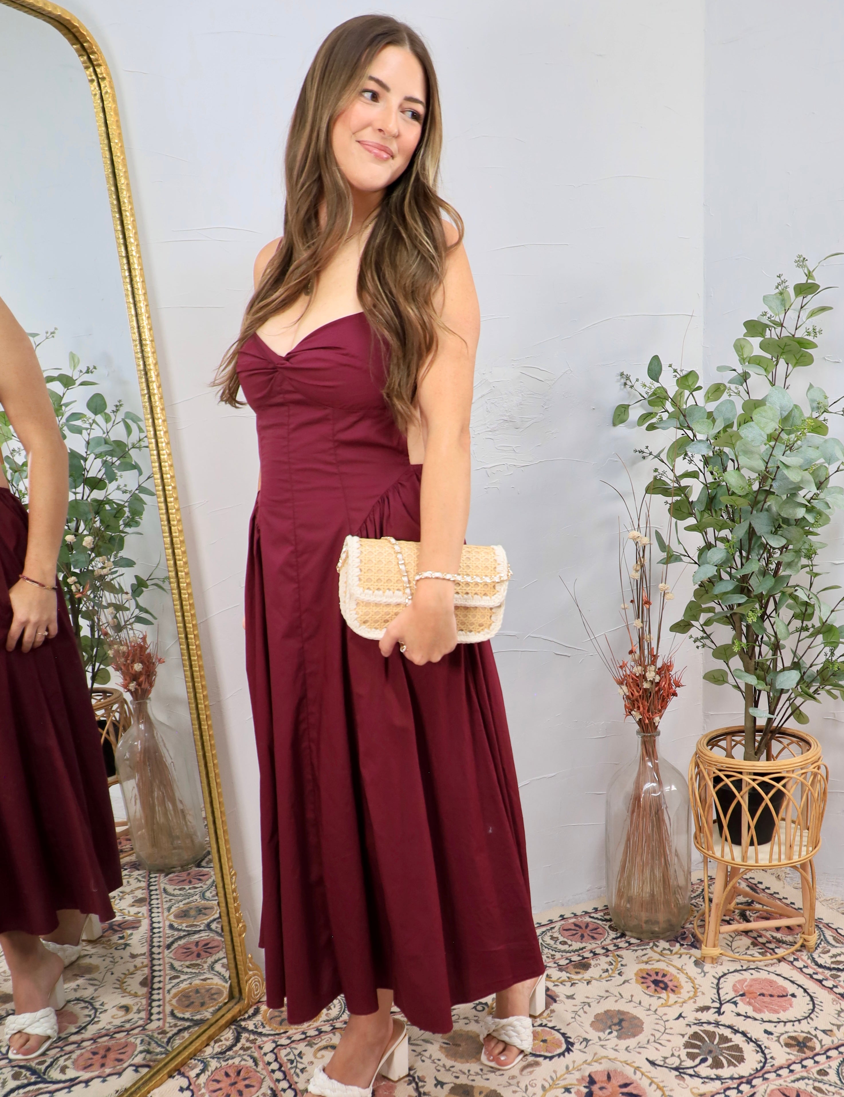 Woman wearing a strapless plum midi dress with sweetheart neckline and woven clutch