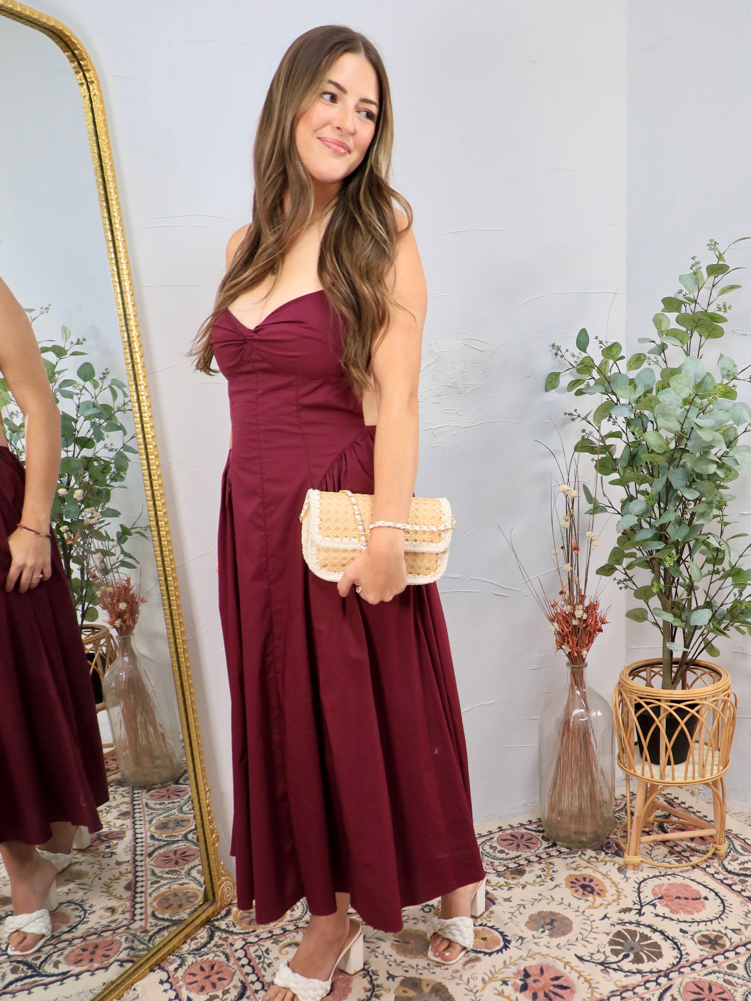 Woman wearing a strapless plum midi dress with sweetheart neckline and woven clutch