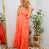 Woman wearing a vibrant coral tiered maxi dress with spaghetti straps and white platform sandals