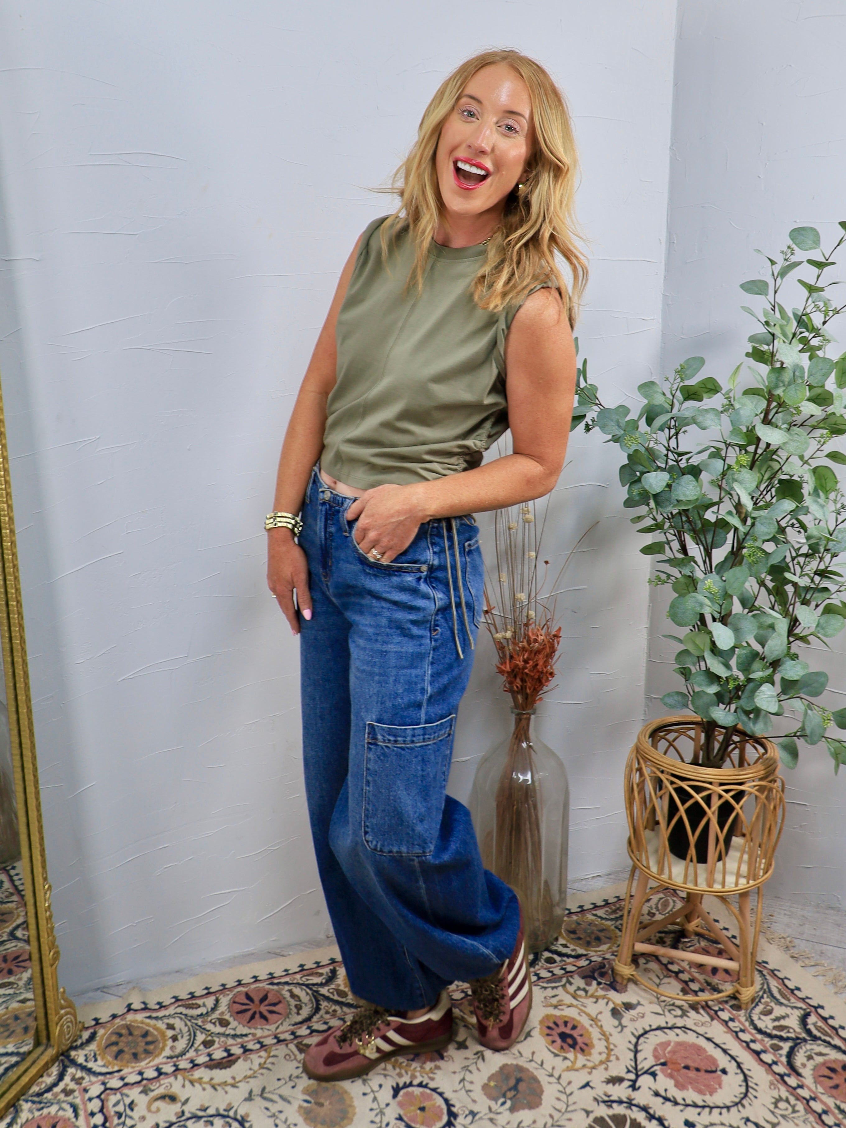 Mid-rise wide-leg cargo denim jeans in medium blue wash, styled with olive sleeveless top and sneakers.