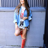 Woman wearing oversized light wash denim shirt layered over graphic tee and cow print mini skirt with red cowboy boots