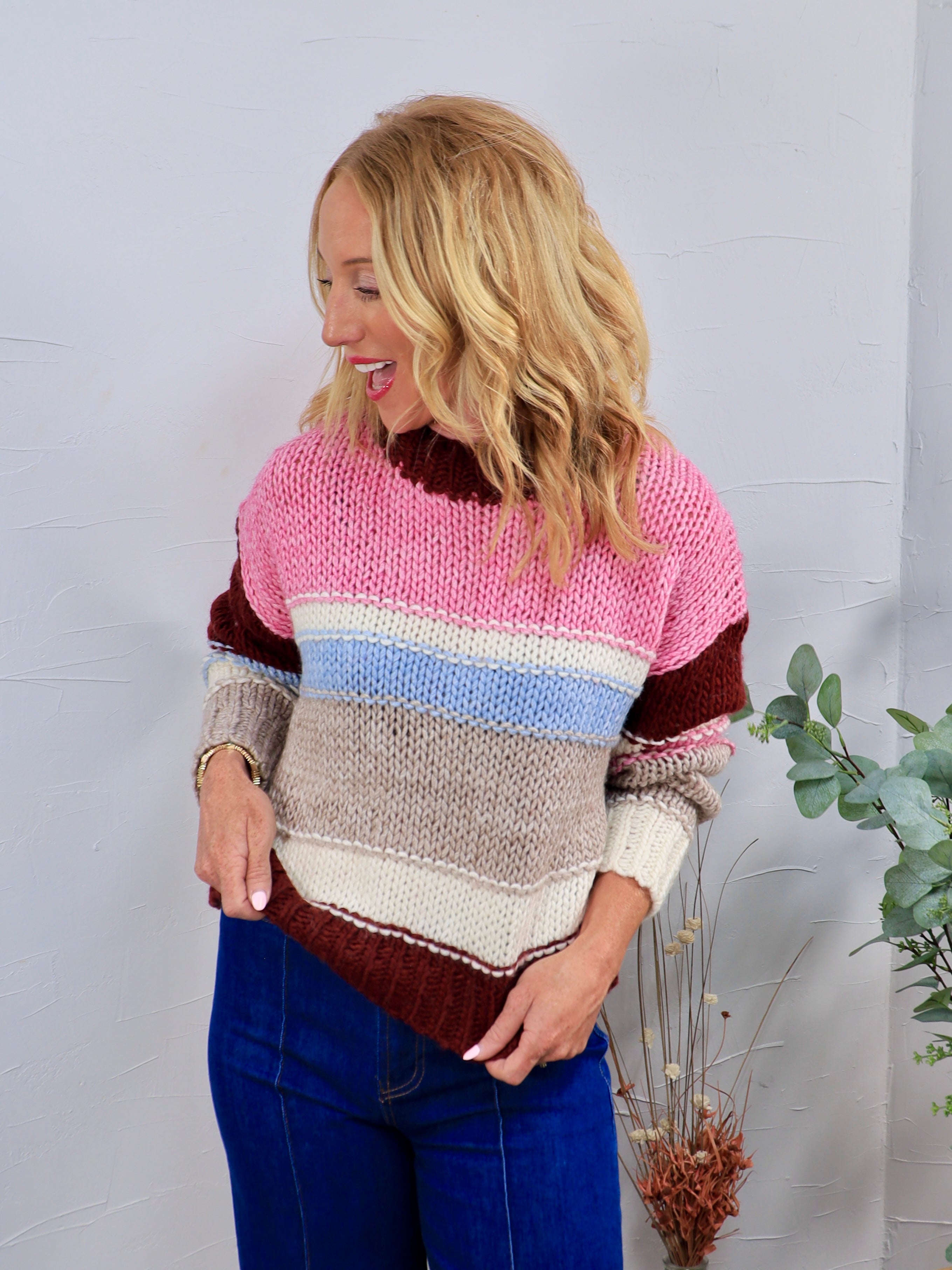 Chunky knit striped crewneck sweater in pink, burgundy, blue, and gray, styled with blue jeans.