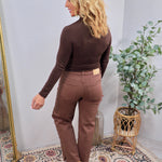 Brown studded straight-leg denim jeans styled with dark brown turtleneck bodysuit and tan cowboy boots, back view.