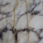 Gold rolo chain necklace with emerald green baguette stones and clear crystal accents on marble surface