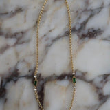 Gold rolo chain necklace with emerald green baguette stones and clear crystal accents on marble surface