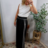 White sleeveless mock-neck top styled with black wide-leg trousers and white trim belt detail.
