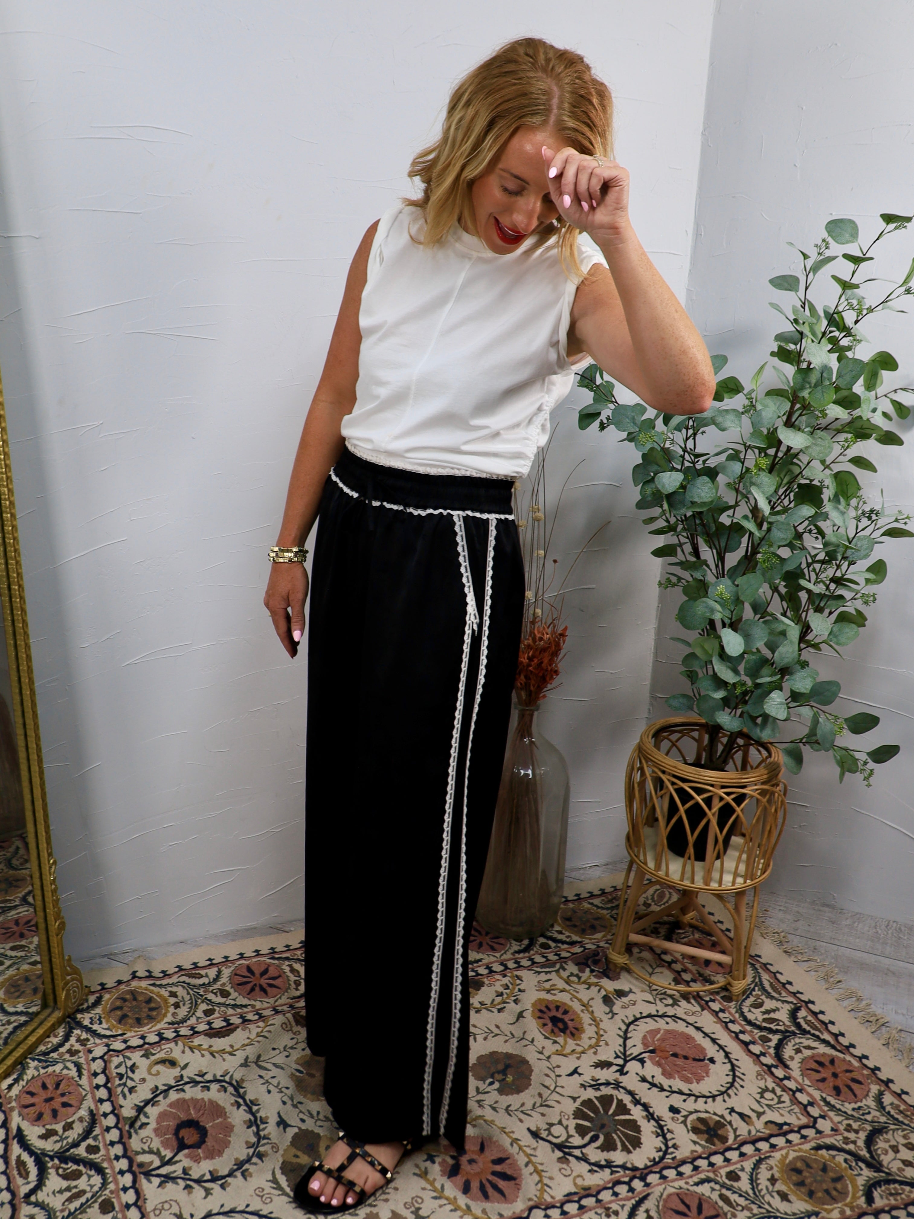White sleeveless mock-neck top styled with black wide-leg trousers and white trim belt detail.