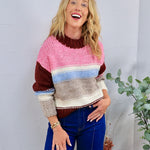 Chunky knit striped crewneck sweater in pink, burgundy, blue, and taupe, styled with dark blue jeans.