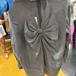 Gray houndstooth patterned blouse with large bow detail at front, long sleeves, being held up in store setting.