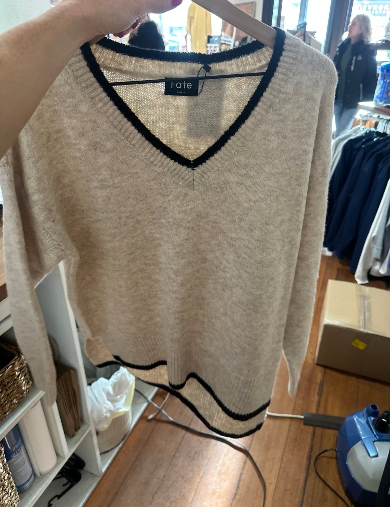 Beige v-neck sweater with black contrast trim detail on hanger in boutique