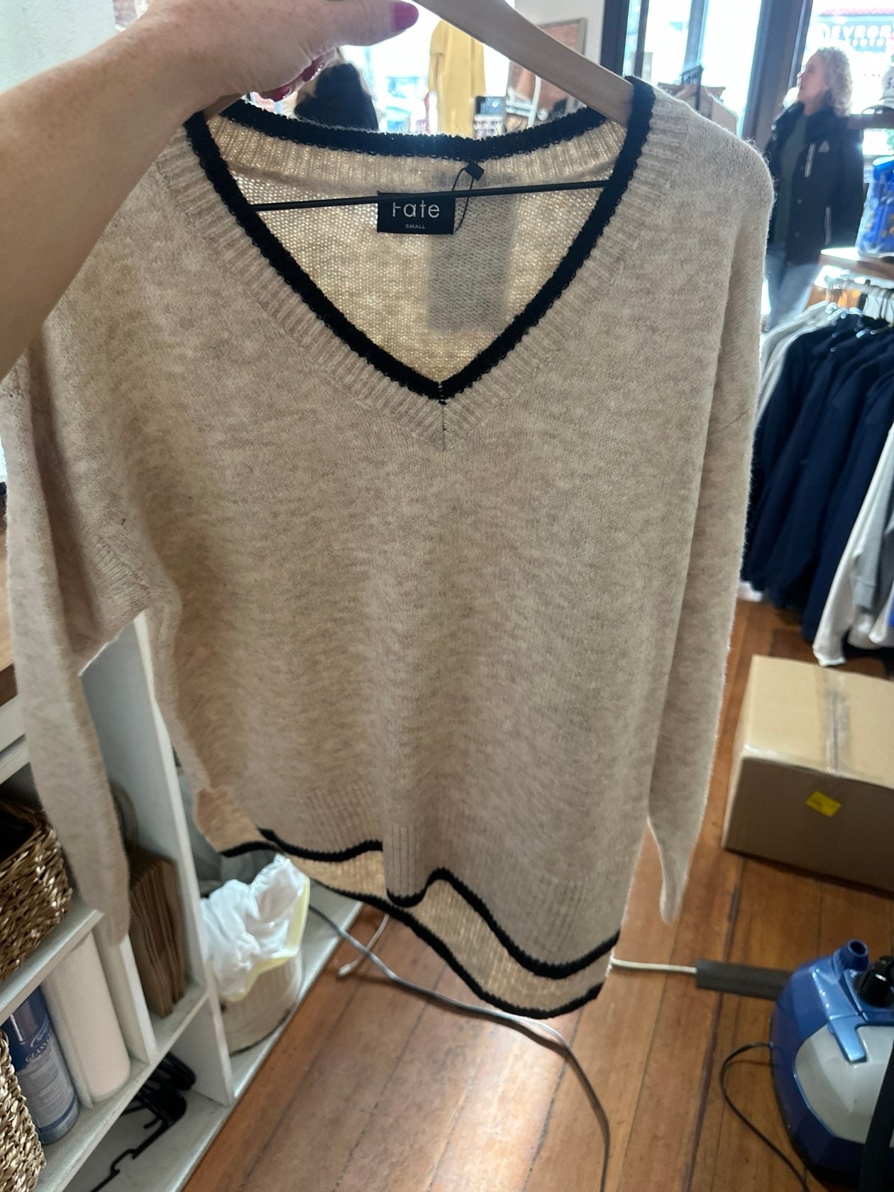 Beige v-neck sweater with black contrast trim detail on hanger in boutique