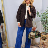 Woman wearing oversized dark brown utility shacket over cream blouse with wide-leg jeans and camo bag