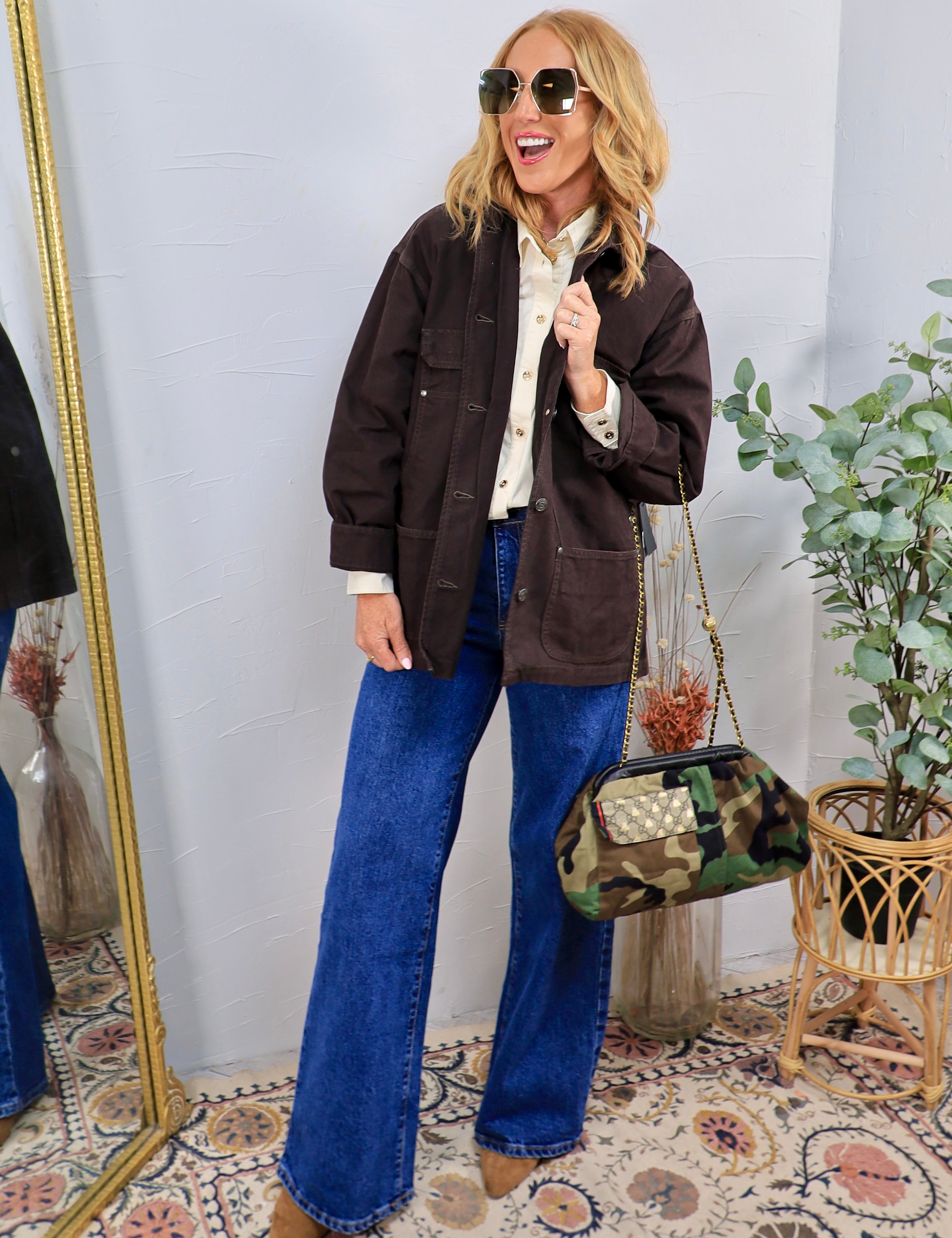 Woman wearing oversized dark brown utility shacket over cream blouse with wide-leg jeans and camo bag