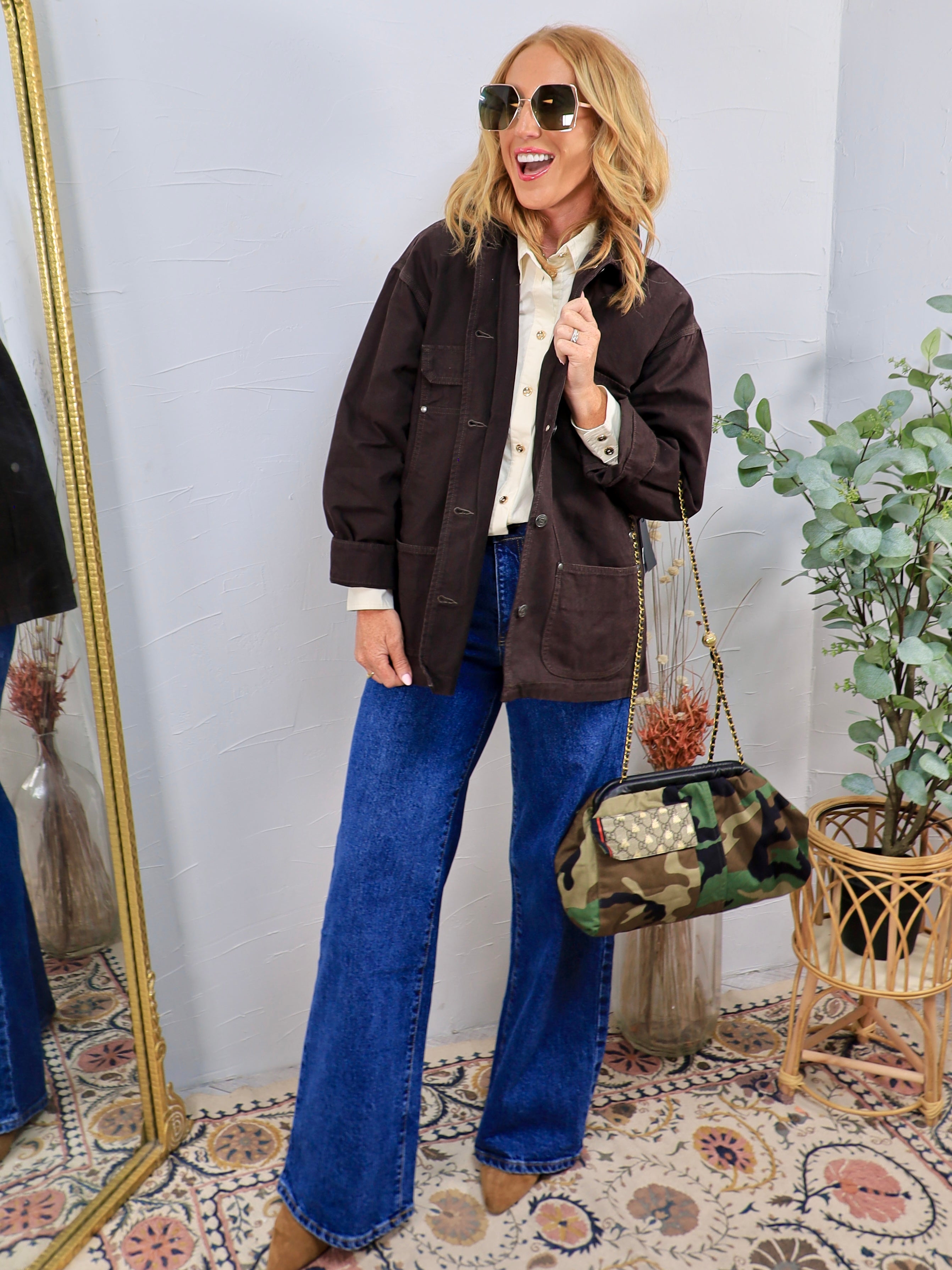 Woman wearing oversized dark brown utility shacket over cream blouse with wide-leg jeans and camo bag