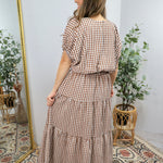 Woman wearing brown and white gingham checkered tiered midi dress with short sleeves, cinched waist, and ruffled layers.