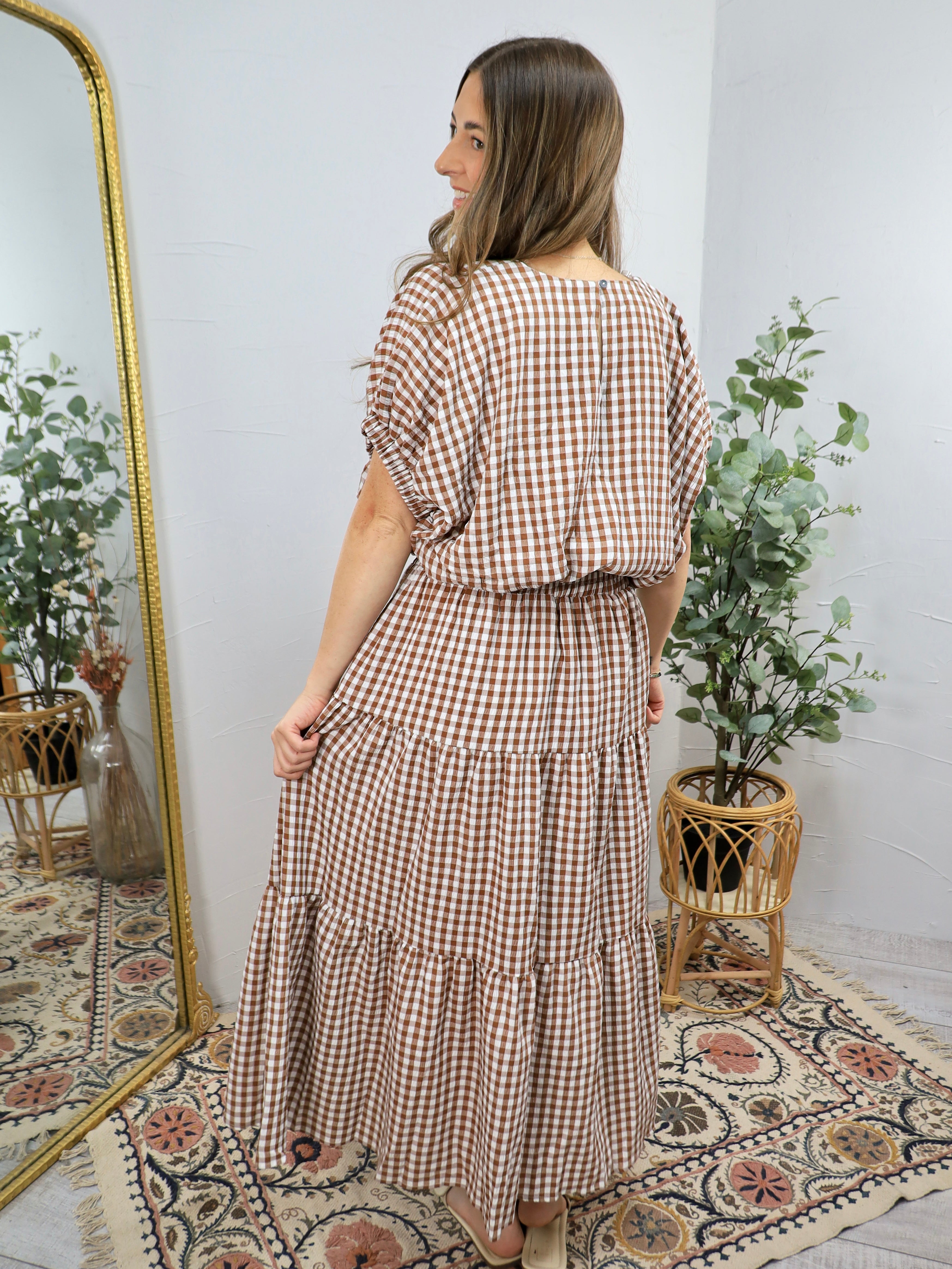 Woman wearing brown and white gingham checkered tiered midi dress with short sleeves, cinched waist, and ruffled layers.