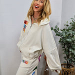 White joggers with colorful rainbow "HO HO HO" embroidered lettering, styled with matching zip-up hoodie set.