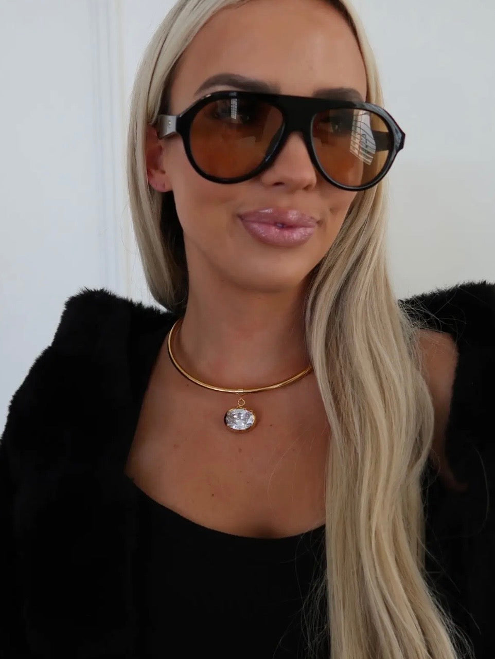 Gold rigid choker necklace with large oval crystal pendant worn close to the neck