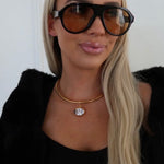 Gold rigid choker necklace with large oval crystal pendant worn close to the neck