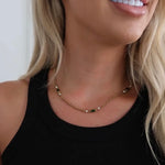 Gold chain necklace with green baguette stones and crystal accents, worn on a model in a black tank top.