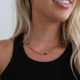 Gold chain necklace with green baguette stones and crystal accents, worn on a model in a black tank top.