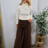 White ribbed turtleneck long sleeve top styled with wide-leg brown pants and tan boots.