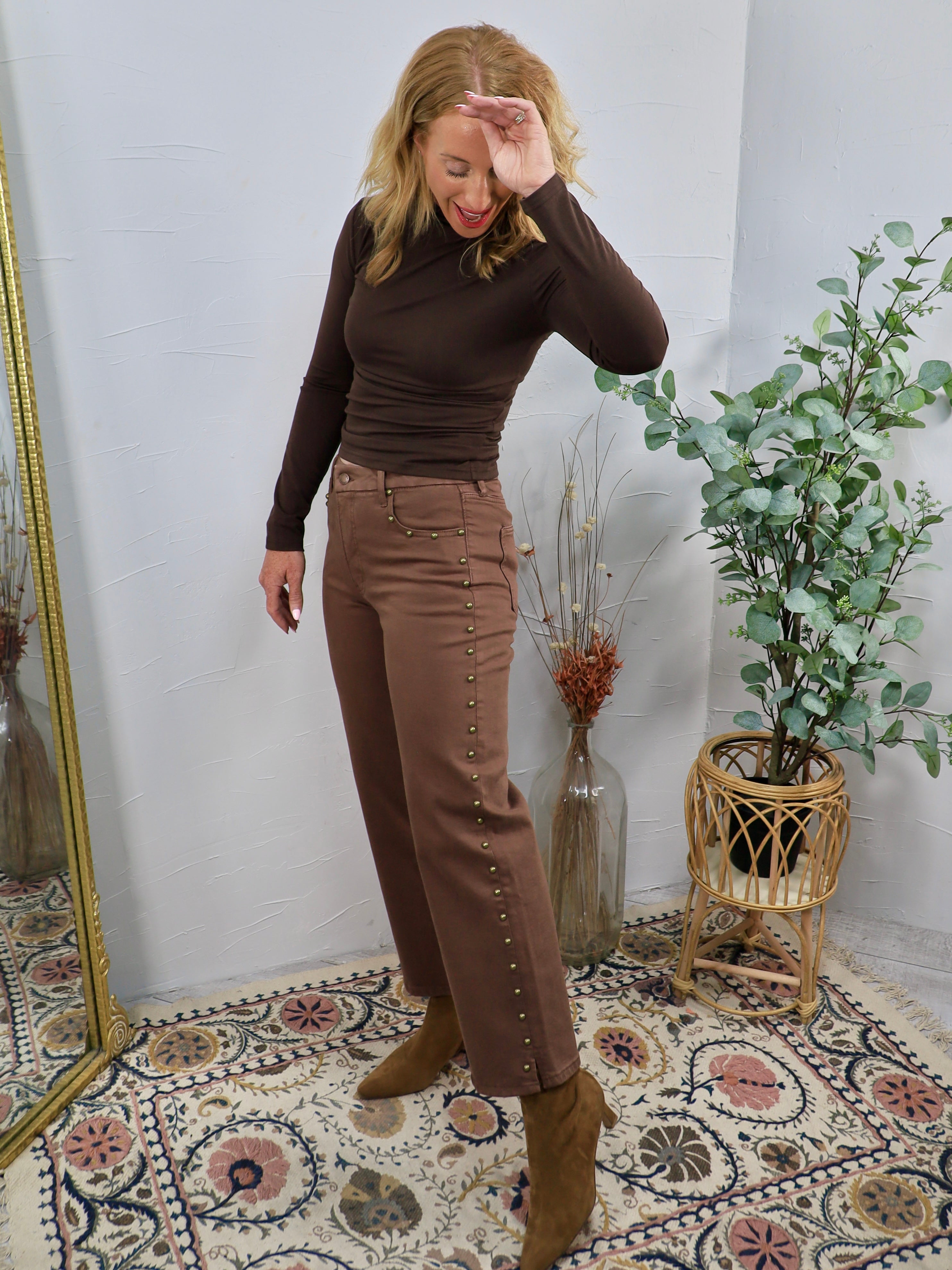 Brown studded straight-leg denim jeans styled with dark brown turtleneck and tan ankle boots.
