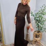 Dark brown pleated maxi skirt styled with matching brown turtleneck top, floor-length silhouette, worn by blonde model.