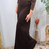 Woman wearing a chocolate brown ribbed pleated maxi skirt with a fitted long-sleeve top and tan flats