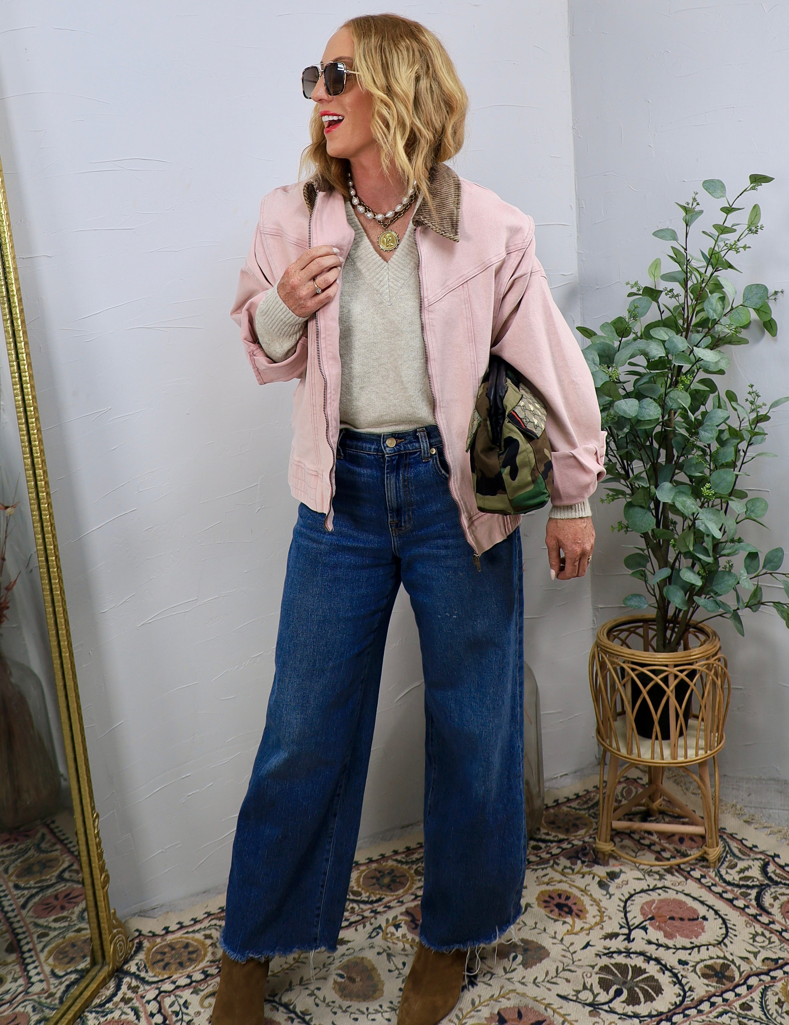 Woman wearing a dusty rose zip-up bomber jacket with corduroy collar, wide-leg jeans, and ankle boots