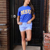 Blue MSU graphic tee with gold lettering, styled with blue gingham lace-trim shorts and white sneakers.