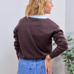 Brown knit sweater layered over light blue collared shirt, paired with blue jeans, back view.