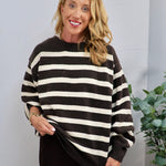 Dark brown and cream striped oversized crewneck sweater with ribbed cuffs, styled casually on a smiling blonde model.