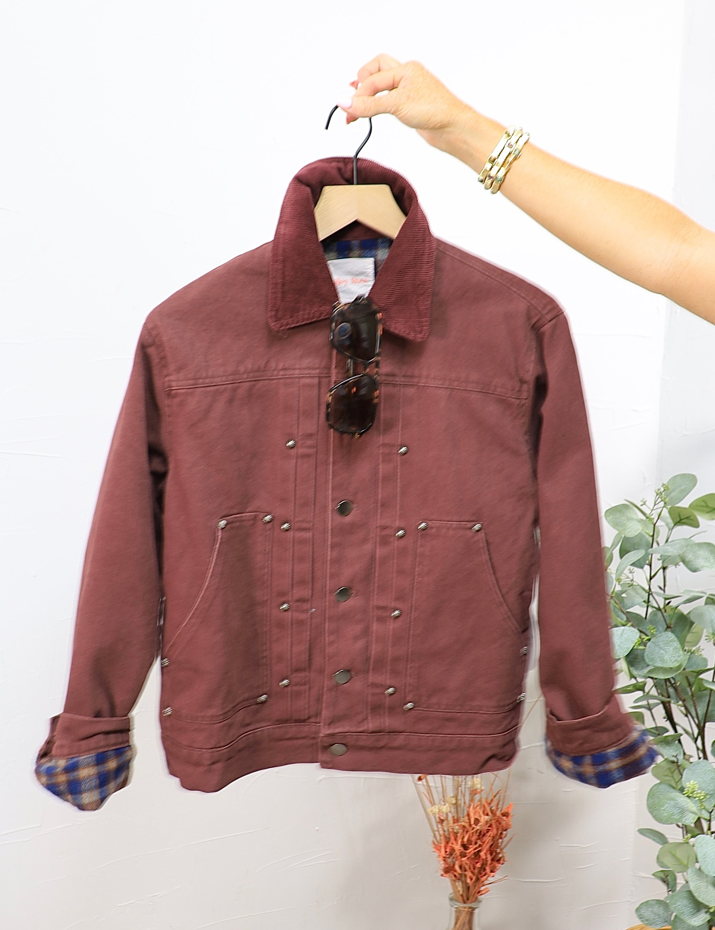 Burgundy snap-button trucker jacket with plaid flannel lining and corduroy collar on wooden hanger
