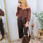 Dark brown faux leather wide-leg pants styled with paisley off-shoulder top, brown boots, and matching tote bag.