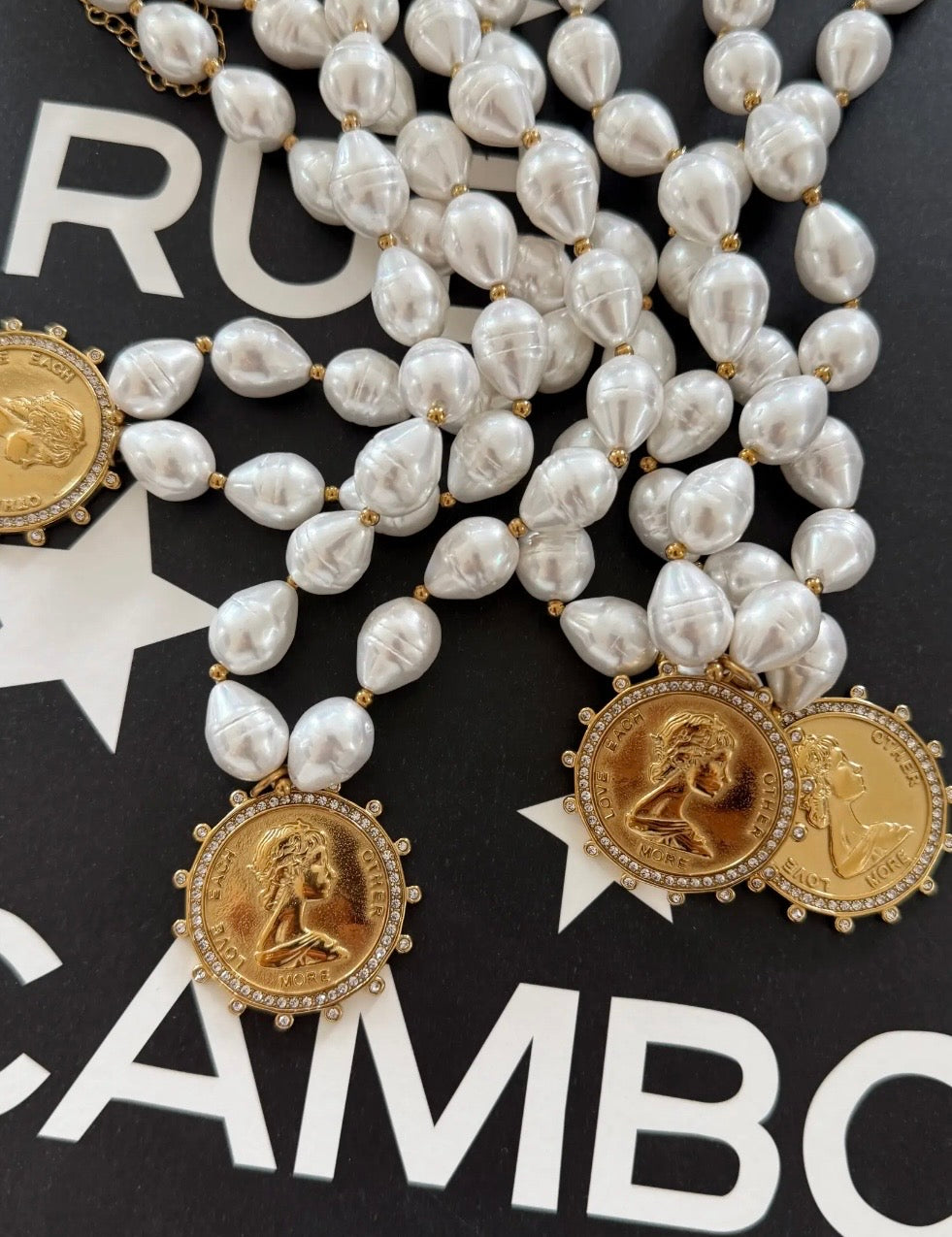 Pearl beaded necklace with gold coin pendants engraved "Love Each Other More," crystal-encrusted borders.