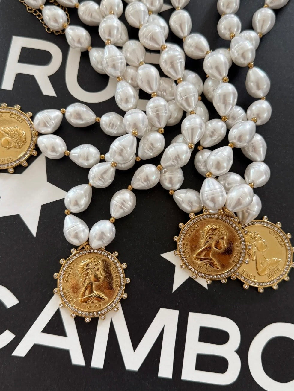 Pearl beaded necklace with gold coin pendants engraved "Love Each Other More," crystal-encrusted borders.