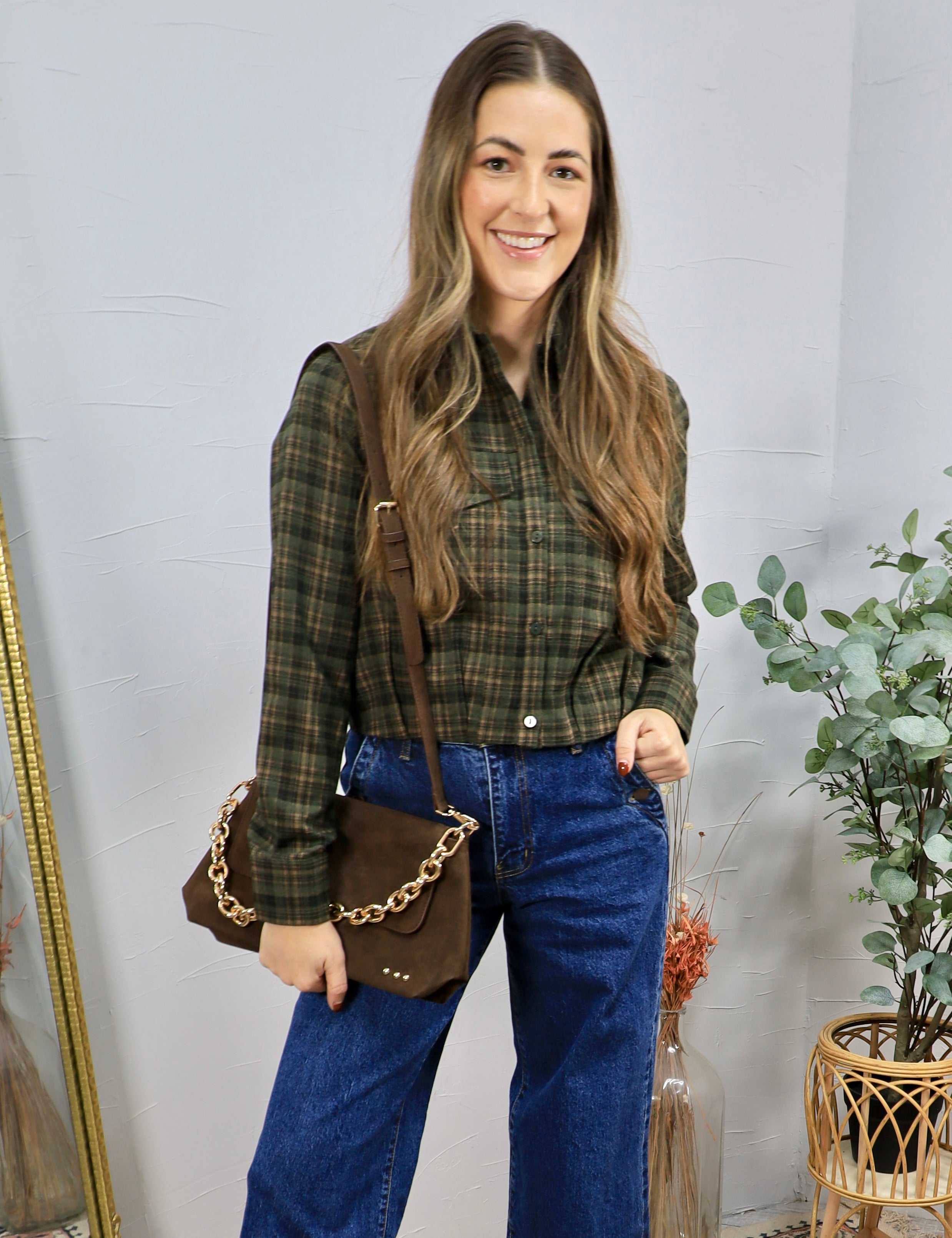 Woman wearing olive green plaid cropped button-up shirt with wide-leg blue jeans and brown crossbody bag