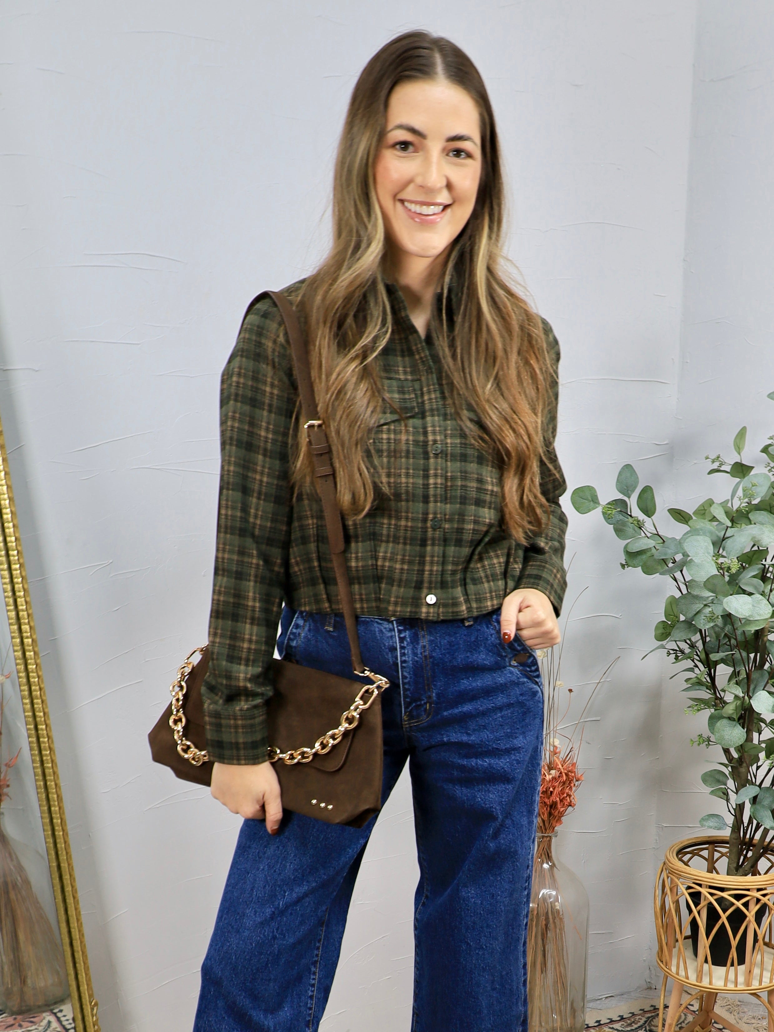 Woman wearing olive green plaid cropped button-up shirt with wide-leg blue jeans and brown crossbody bag